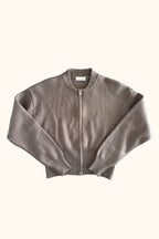 A cropped, long-sleeve knit zip-up cardigan in a muted taupe-brown color, featuring ribbed collar, cuffs, and hem, with a silver-tone zipper.