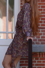 woman with red hair leaning against a stair railing and wearing a wrap mini dress with paisley print