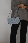 A person wearing a gray sweater and black pants carries a light blue suede shoulder bag with gold-tone hardware and a flap closure.