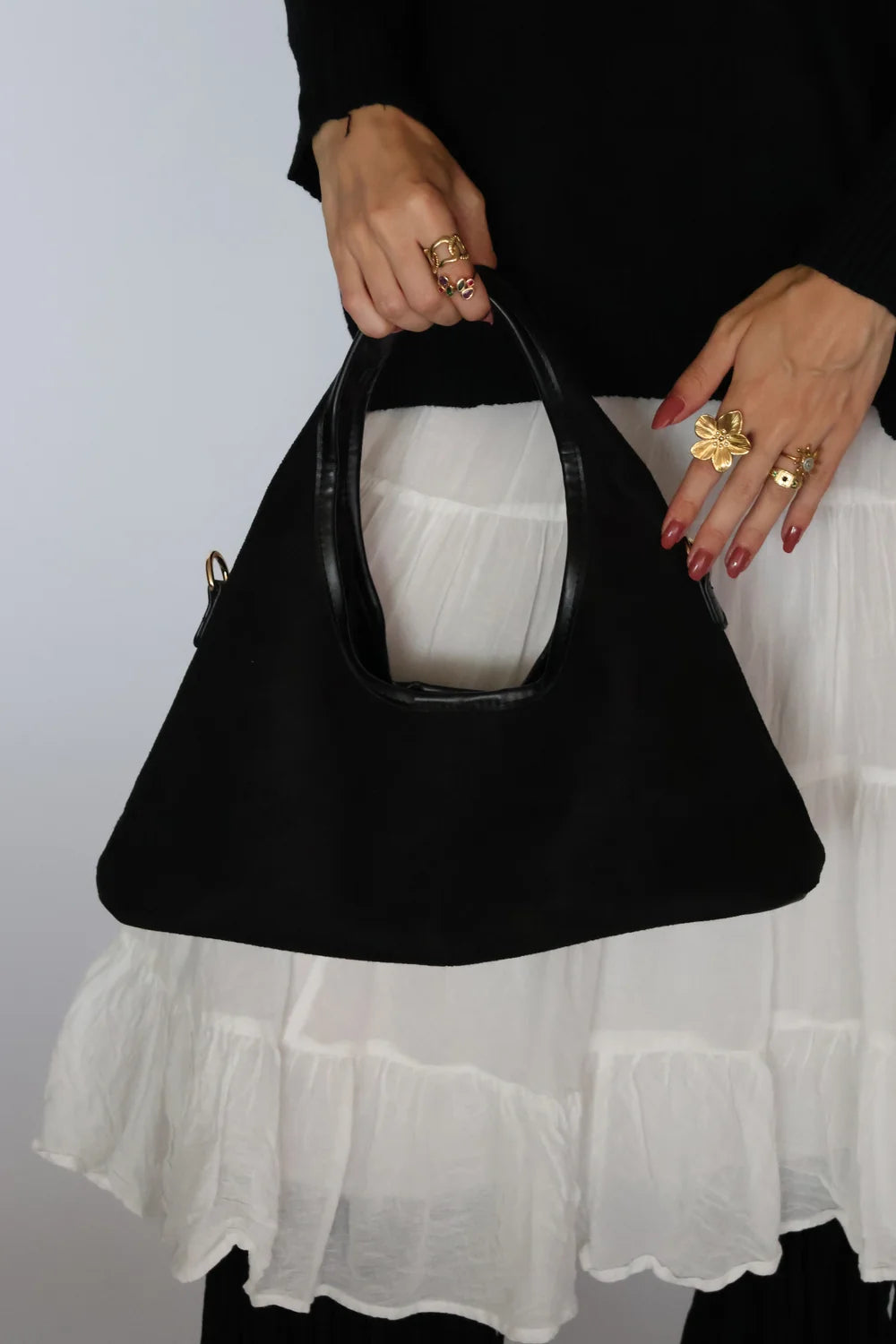 woman wearing a white skirt, black sweater, and black boots, and a black suede hobo bag